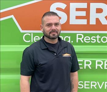 Jorge standing in front of a vehicle with a logo behind him