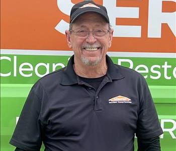 Male Employee with black polo standing in front of tan background