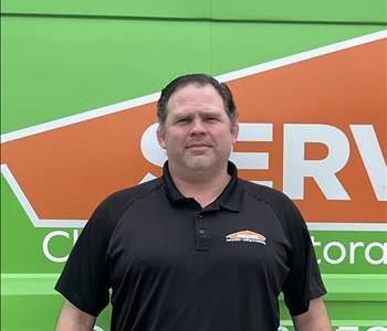 Male Employee with black polo standing in front of tan background