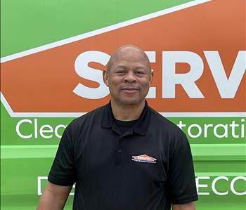 Male Employee with black polo standing in front of tan background