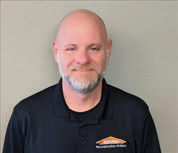 Male Employee with black polo standing in front of tan background